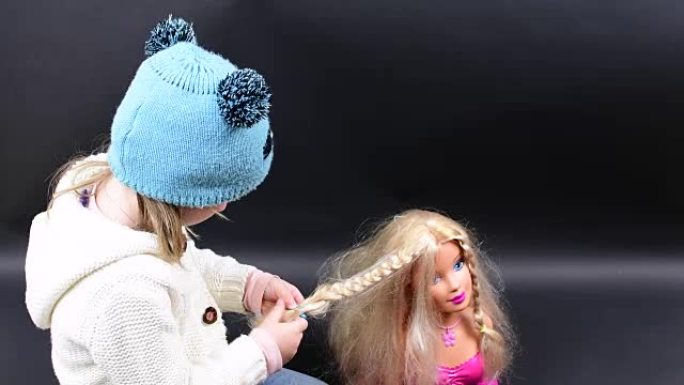 可爱的女孩梳子造型头。小女孩穿着冬装。黑色背景上可爱的小女孩。
