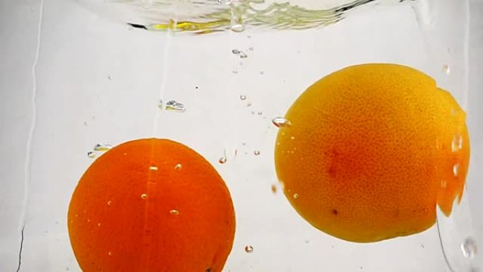 整个葡萄柚，橙子和柠檬随着气泡落入水中。慢动作的柑橘类水果视频。