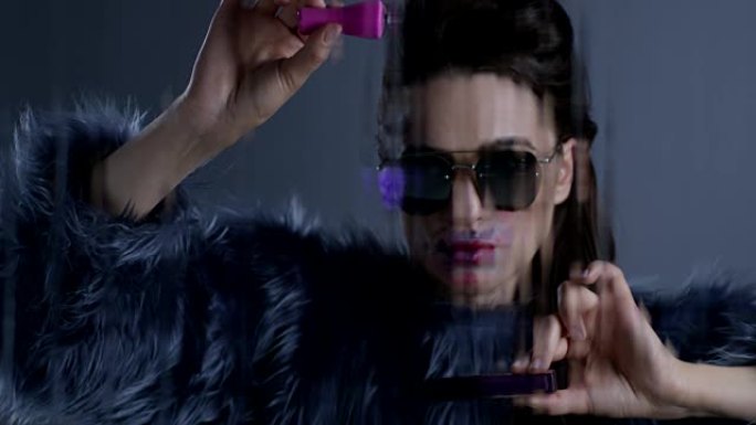戴着太阳镜和皮草的黑发高级时装模特一只手拿着粉色指甲油，另一只手拿着紫色唇膏。时尚视频。