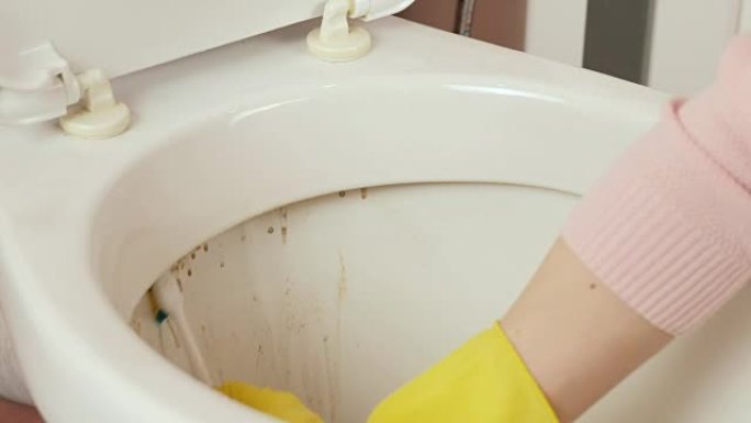 妇女的双手特写黄色橡胶手套用海绵洗马桶。顶视图。