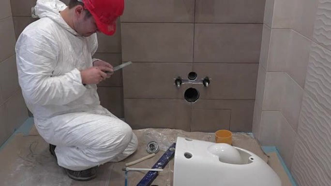 熟练的水管工在新的现代浴室中从事马桶手座的工作