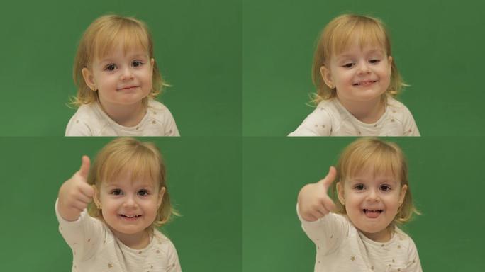 竖起大拇指。好的。两岁的漂亮女孩。可爱的金发孩子。棕色的眼睛。特写。绿屏背景
