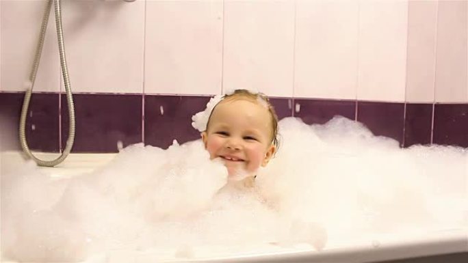 快乐的小女孩用泡沫在浴室洗澡。他玩泡沫