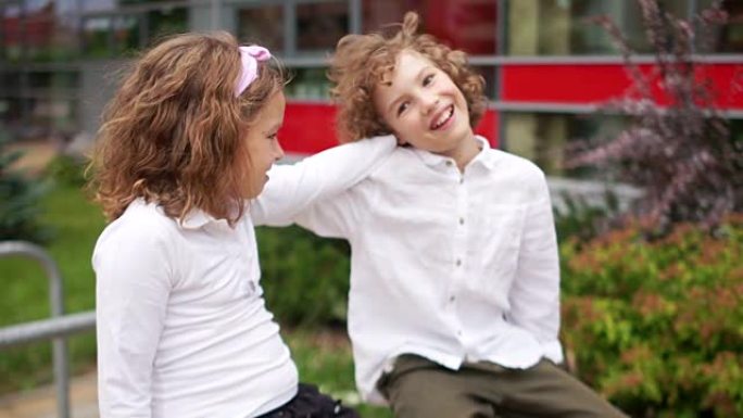 学校友谊。一对少年，一个男孩和一个女孩坐在栏杆上，女孩把手放在男孩的肩膀上。穿着白衬衫的孩子们