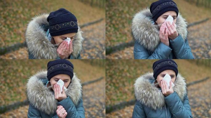 一个女人在秋天的公园打喷嚏，感冒了。