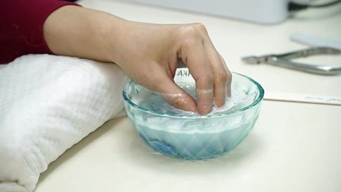 美甲美容院。美甲师制作指甲护理程序。程序保湿指甲，手放在浴缸里用水。特写