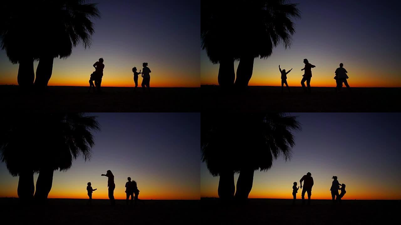 美丽的热带日落。一家四口在棕榈树下的海滩上跳舞。