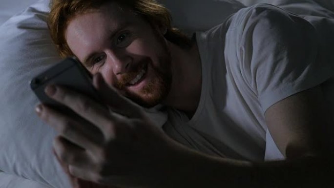 红发胡子男人晚上在智能手机上进行在线视频聊天