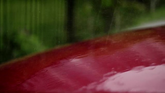 从外面看，有大雨，阵雨，大水滴落下，水花飞溅，在红色空车引擎盖的潮湿表面上站在停车场