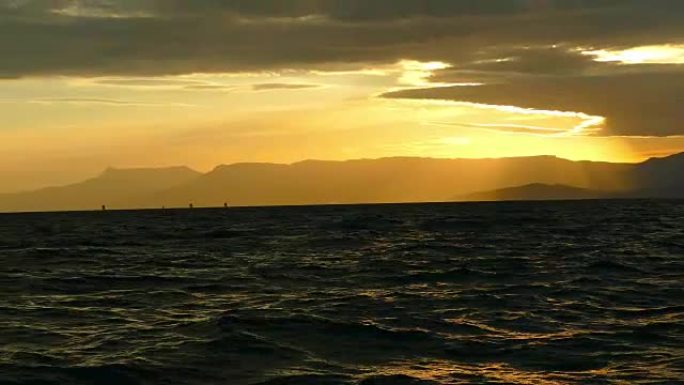 日落时山脉海岸背景上的帆船赛