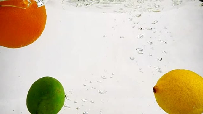 柠檬、橙子和酸橙落入水中。孤立背景上有气泡的慢动作水果。