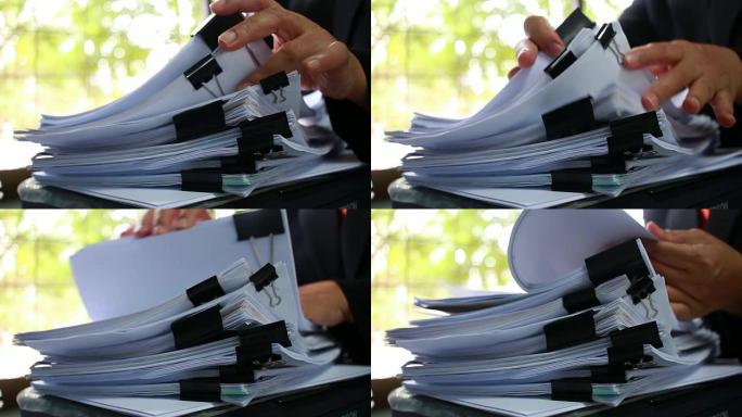 商人手在办公桌上搜索未完成的文档堆叠的纸质文件以获取报告文件，在桌子上用夹子将纸张成堆，文件书写，绘