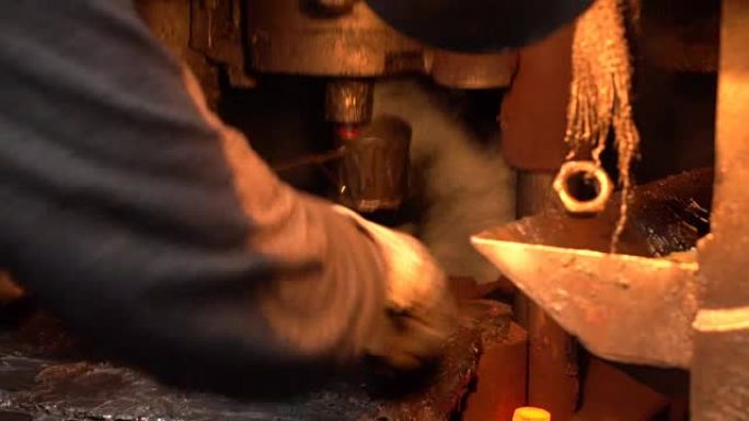 铁匠工人用钳子在锻压机下换红色铁锭