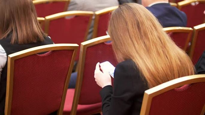 在商务会议上，人们坐在红色椅子上的大厅里，手握智能手机的女性