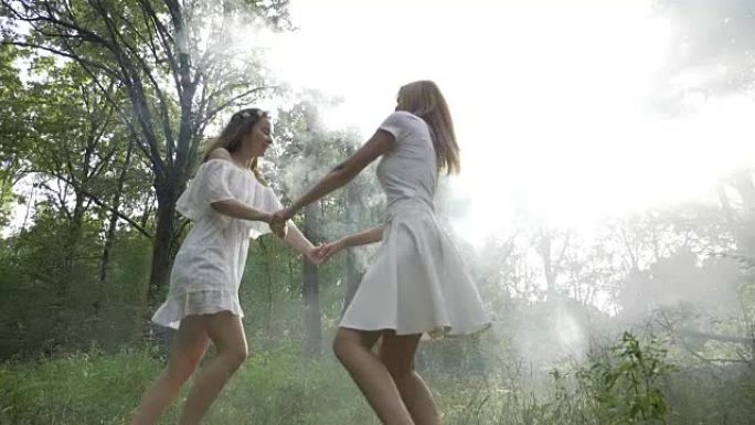 两个美丽的朋友在慢动作的烟雾中在草地上旋转和跳舞
