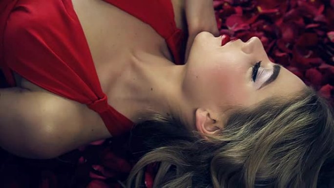 穿着红色连衣裙的女孩，有着美丽的发型，躺在红玫瑰的花瓣中