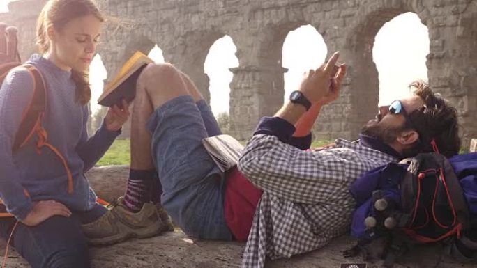 幸福的年轻夫妇背包客游客坐在原木后备箱上阅读书籍，在罗马parco degli acquedotti