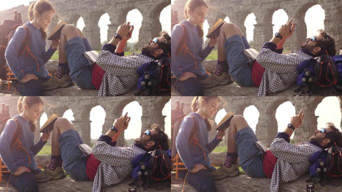 幸福的年轻夫妇背包客游客坐在原木后备箱上阅读书籍，在罗马parco degli acquedotti