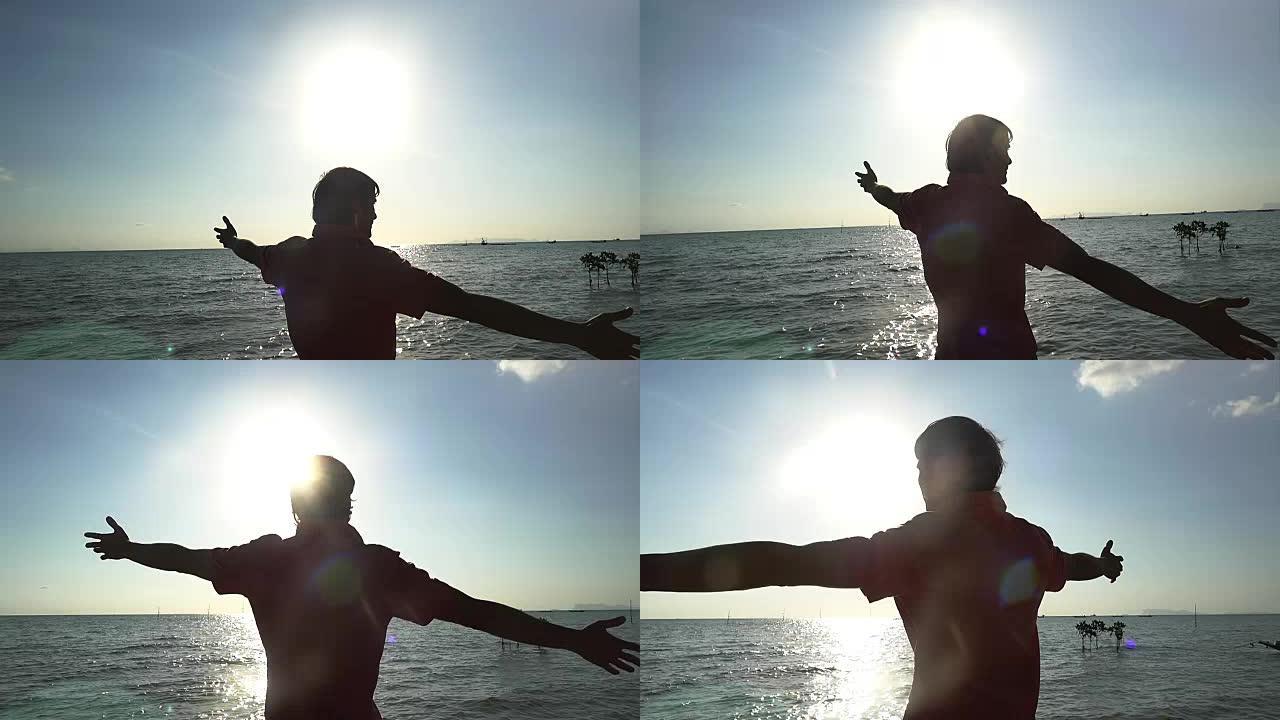 快乐的年轻人在海边的海滩上慢动作举起双手。阳光闪耀着美丽的镜头耀斑效果。1920x1080