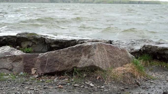 一个穿着牛仔裤站在河里一块岩石上的男人的腿特写。运动鞋踩在石头上。在暴风雨的日子里，水在脚下的特写镜