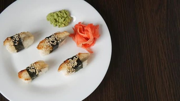 一个大的白色盘子，上面放了四个巨大的寿司，鳗鱼倒出一块紫菜，旁边是粉红色的生姜和绿色的芥末