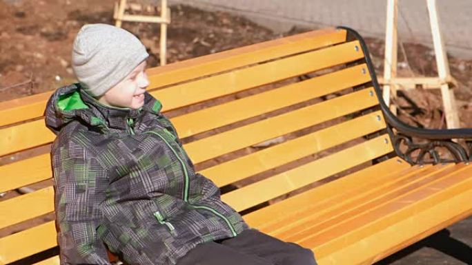 男孩正等着他的父母坐在公园的长凳上。