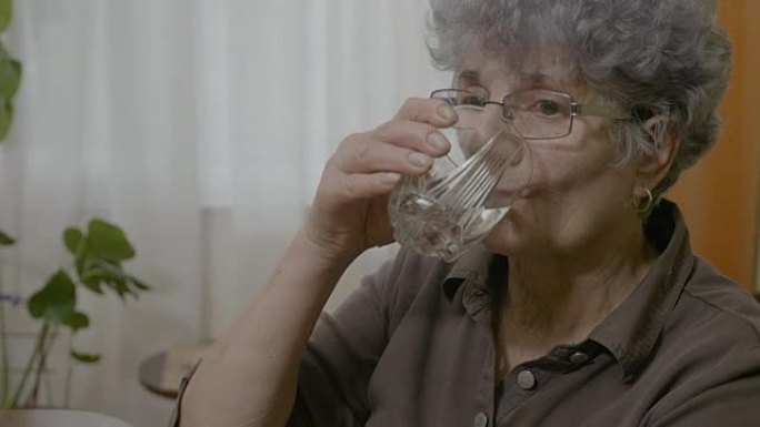 高级老妇服用药丸后吞咽并喝了一整杯水