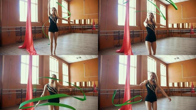 年轻漂亮灵活的女孩用绿丝带训练-在工作室里用镜子做体操，慢动作