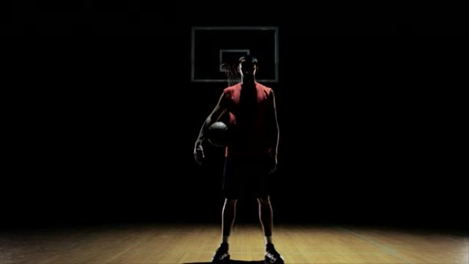 一名篮球运动员运球，然后捡起球，盯着镜头。