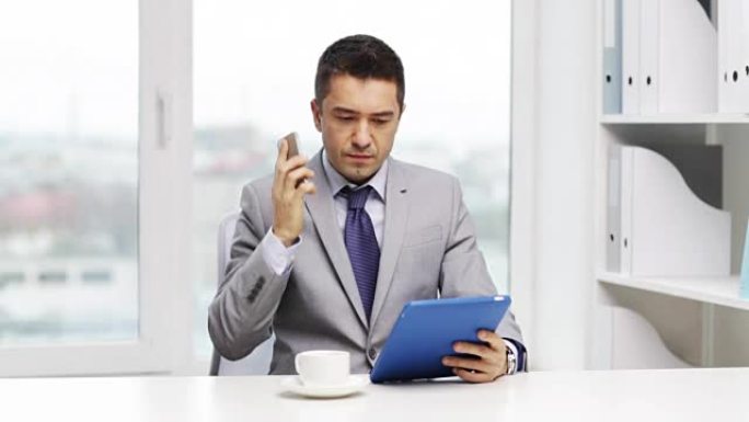 在办公室用平板电脑和咖啡打电话给智能手机的商人