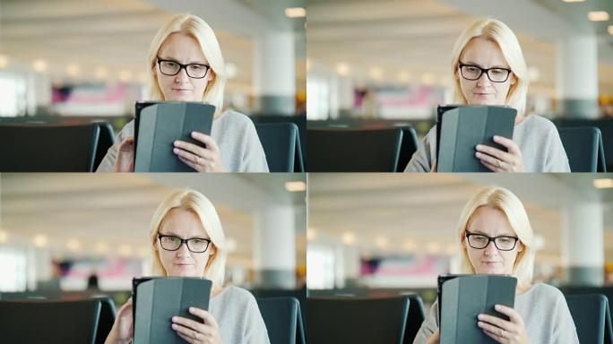 戴眼镜的女人的肖像。坐在汽车站的候车室，使用平板电脑