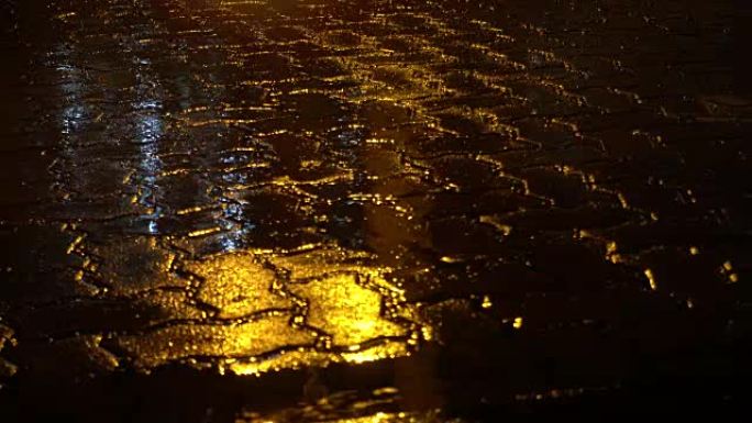 夜街上下雨。水坑中的黄色路灯反射。