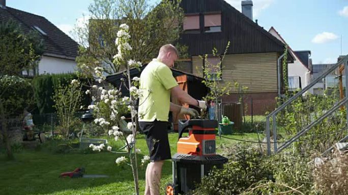 花园里的一个人正在机器上铺设木树枝以切碎。