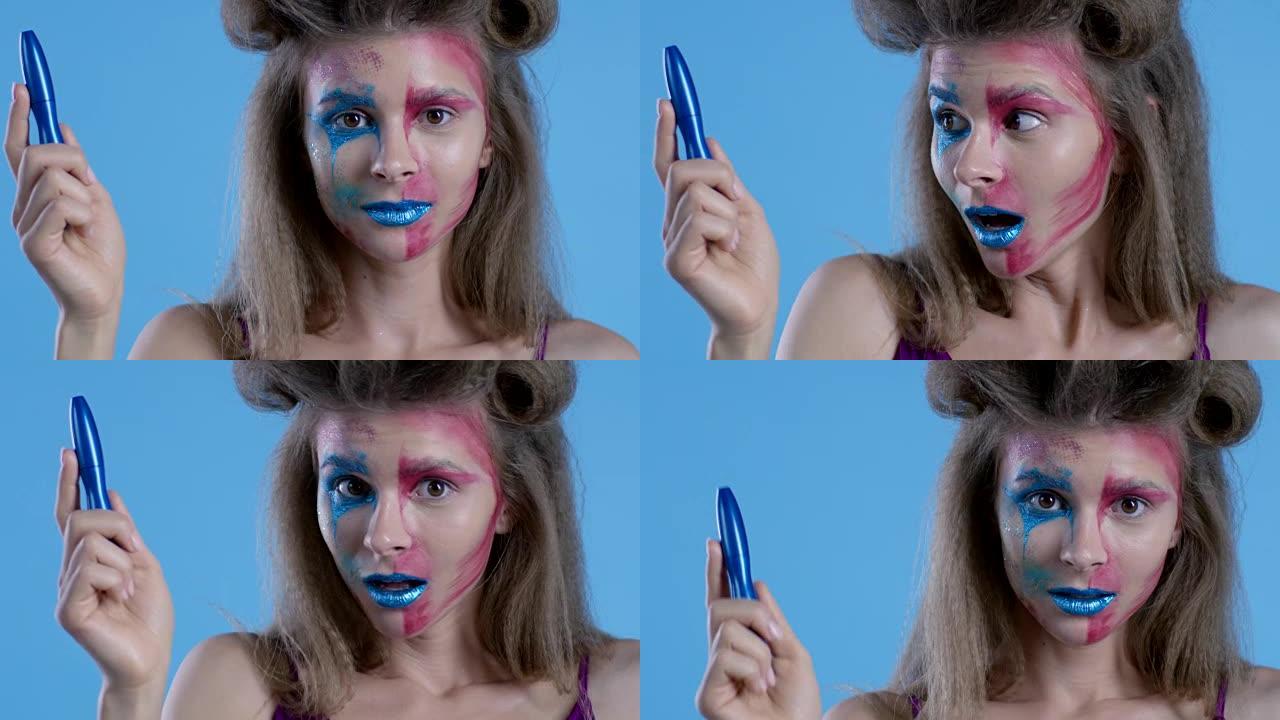 多色舞台化妆的高级时尚金发模特展示蓝色睫毛膏管。时尚视频。