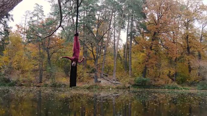 女子杂技演员挂在空中丝绸上，并在森林中表演空中杂技表演