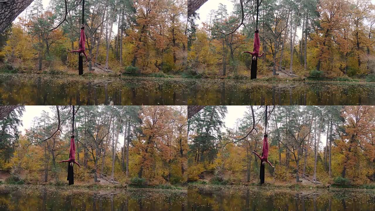 女子杂技演员挂在空中丝绸上，并在森林中表演空中杂技表演