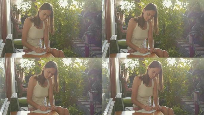 年轻女子坐在阳光下的阳台上，用圆珠笔写日记