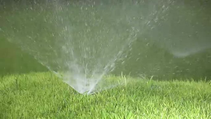 在阳光明媚的日子里，慢动作的自动浇水系统的喷嘴喷嘴的关闭，带有明亮绿色的短毛草坪草