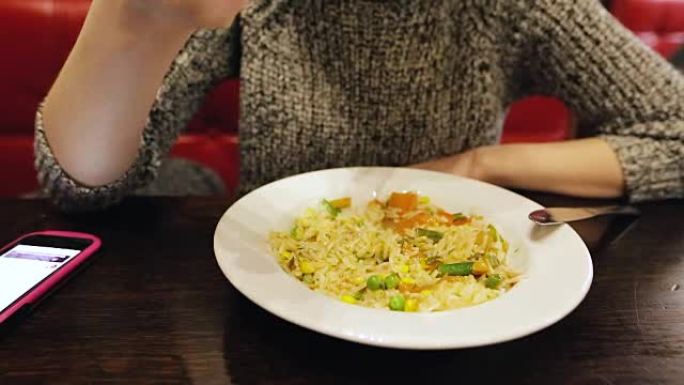 迷人的高加索女孩在咖啡馆用smatphone吃泰国米饭和蔬菜