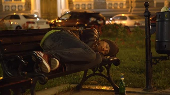 醉汉睡在垃圾桶附近城市的长凳上。