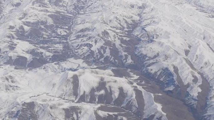 令人惊叹的山脉之美，略被雪覆盖，从云层中掠过，从飞机窗户可以看到