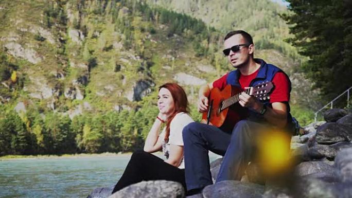 一对夫妇在海边的夏天在山河旁边弹吉他。3840x2160