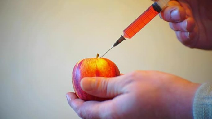 男性双手用注射器注射到成熟的苹果中