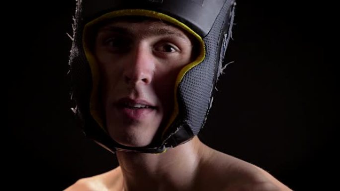 一名年轻的高加索赤裸上身男性疲惫拳击手的肖像，穿着拳击头盔，头部护卫，看着相机，黑色背景50 fps