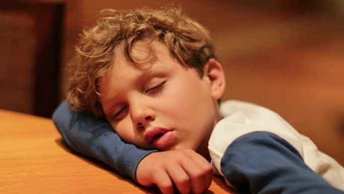 流口水困倦的7岁孩子在桌子上睡着了。经过一整天的活动，筋疲力尽的小男孩休息。表达坦率的真实生活中的孩