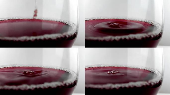 红酒掉落在白色背景上的酒杯中，营养保健概念，慢动作下用高速相机拍摄