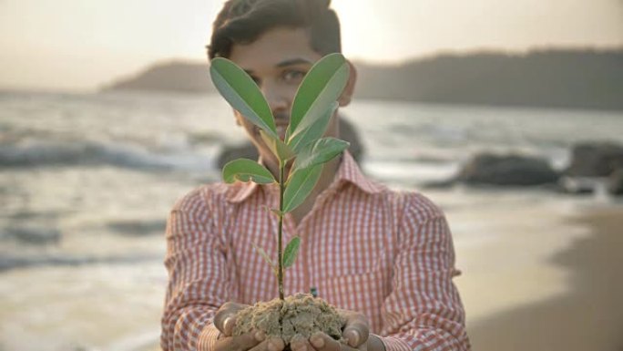 微笑的年轻人或少年双手拿着一棵绿色的小植物或采样