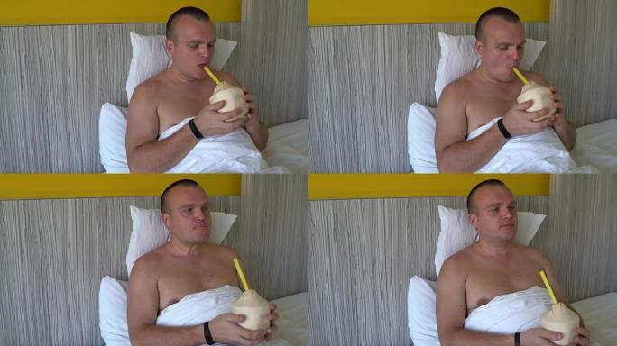 躺在床上的男人通过一根管子从年轻的椰子中喝椰奶