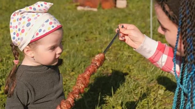 妈妈在后院的肉串上给她可爱的小女儿喂肉。