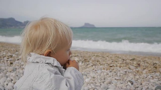 在暴风雨的海浪背景下，白种人金发碧眼的女婴在吃枸杞的果实时含泪。